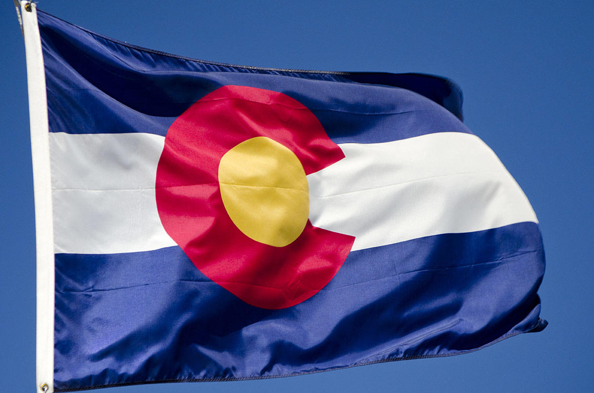 The Colorado state flag flaps in the wind against a blue sky.