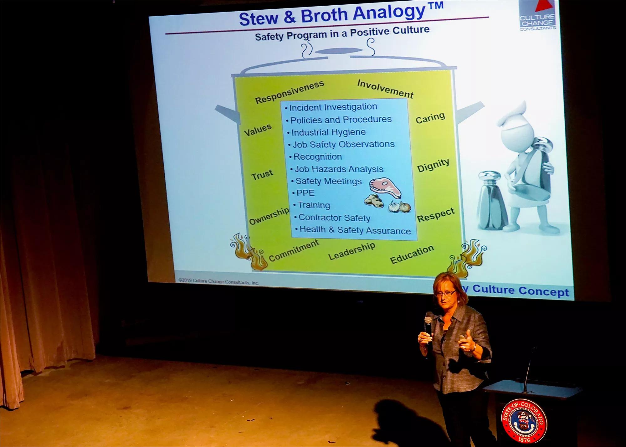 A woman with a microphone speaks in front of a slide about a safety program in a positive culture